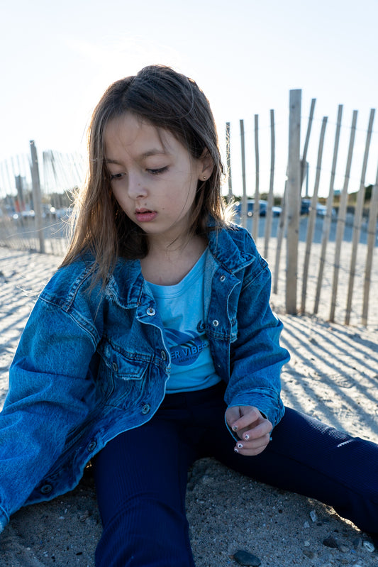 Young woman in blue denim jacket and dark pants sitting on concrete — daring coastal style for risk takers, Sailer's Co. adventure apparel