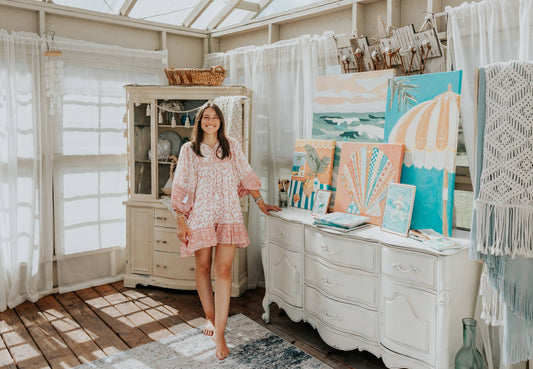 Tianna DeNunzio standing in her art studio among coastal paintings