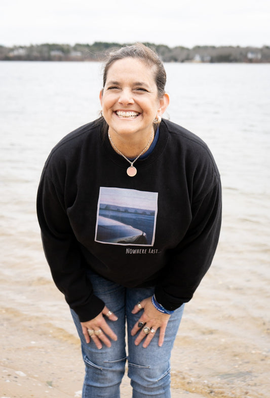 Jennifer Moran laughing on the beach in a black Nowhere Fast sweatshirt