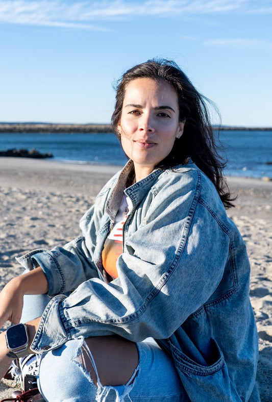 Erika Fernandes-Rusan sitting on the beach in a denim jacket