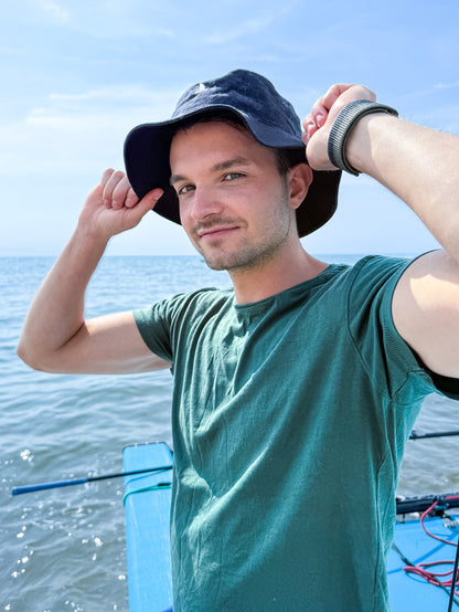 Young man in a black bucket hat and green t-shirt adjusting his hat on a catamaran