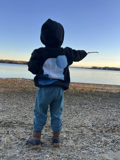 Daring Blues Kids Fleece Hoodie in Black, back view pointing at the water (real photo)