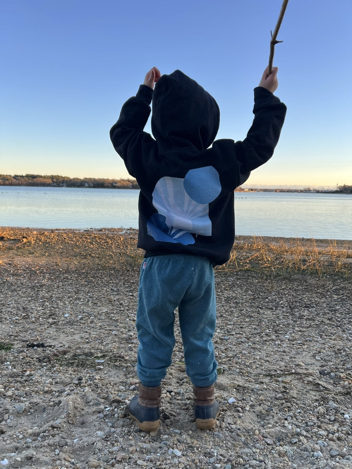 Daring Blues Kids Fleece Hoodie in Black, back view with a stick on the beach (real photo)